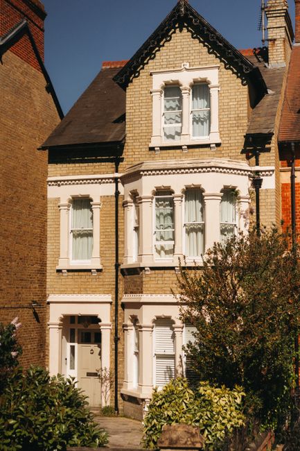 Two movers, wearing navy uniforms and protective eyewear, are loading a large, dark green upholstered piece of furniture into the back of a black moving van parked on a street. The van's rear doors ar